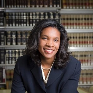 Erika George in formal attire, smiling seated in front of legal volumes